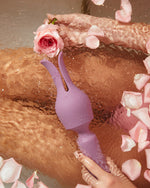 Fioletowy wibrator otoczony płatkami róż i wodą w romantycznej stylizacji fotograficznej