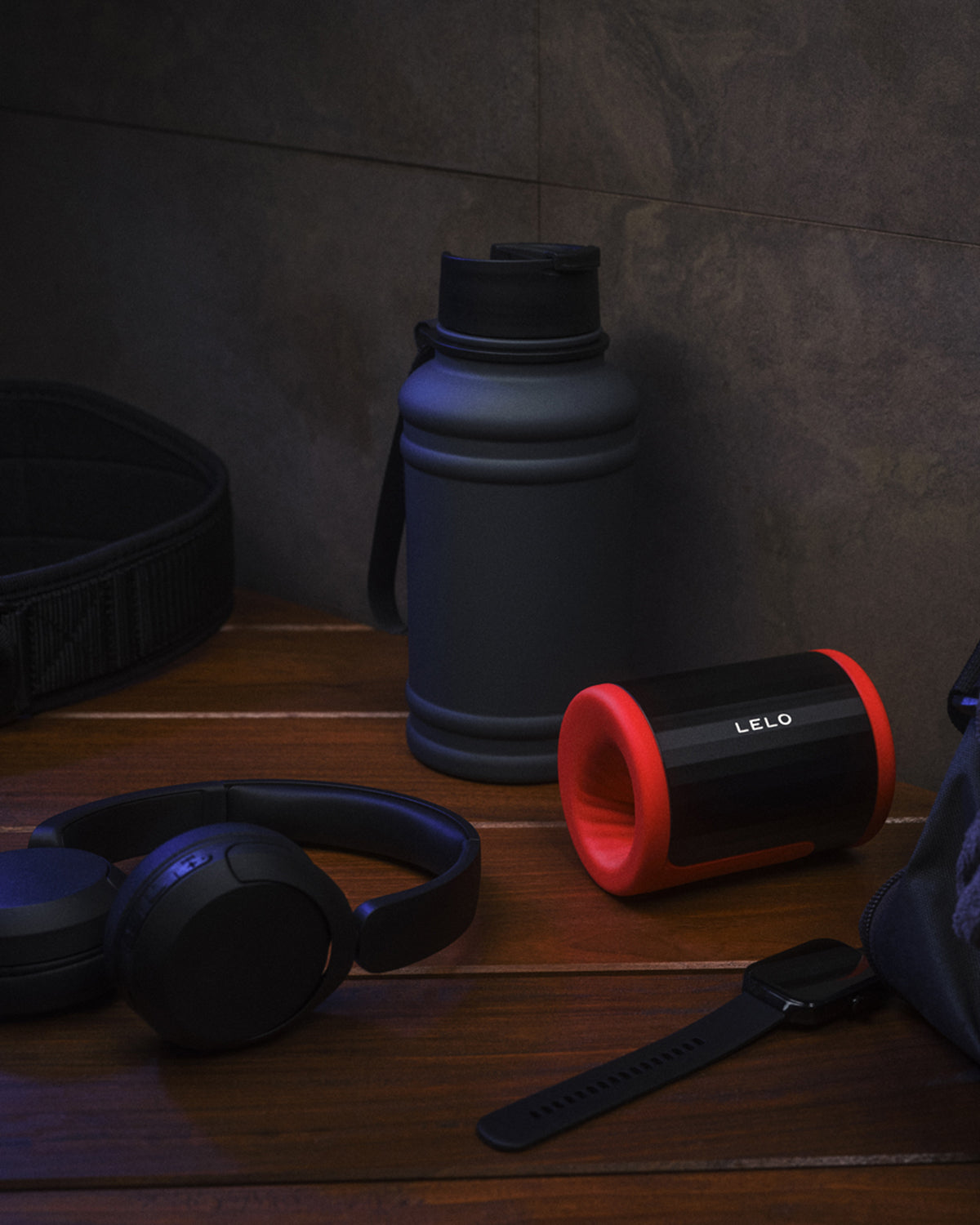 Masturbator LELO F2S - na drewnianej powierzchni obok słuchawek i smartwatcha - kolor czerwony