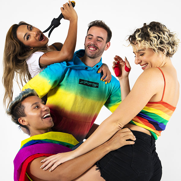 Grupa osób w tęczowych ubraniach, jedna kobieta trzyma masażer łechtaczki. Odkryj specjalnie dobrane produkty dla LGBTQ, w tym akcesoria dla różnych orientacji i identyfikacji.