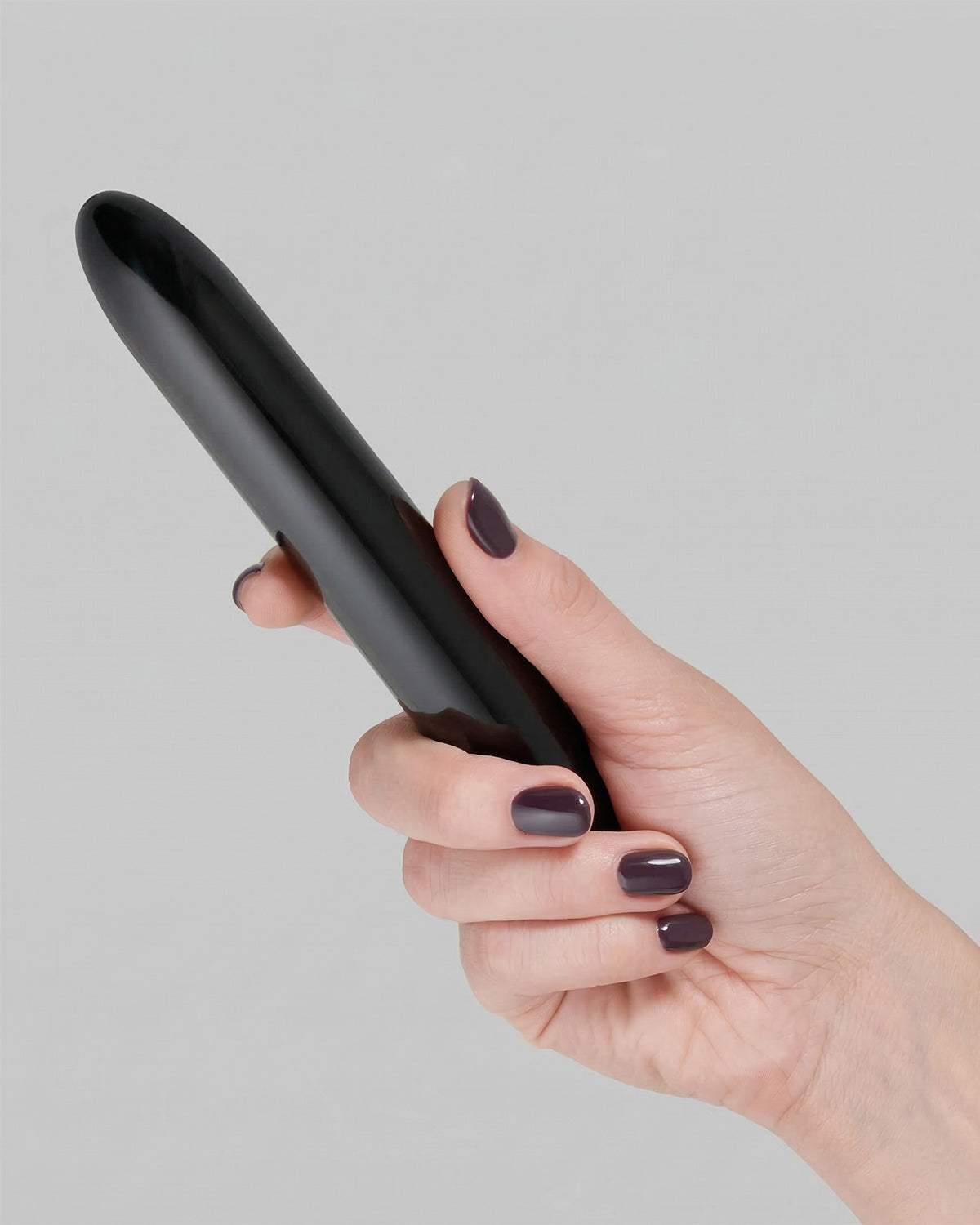 Dłoń trzymająca czarny vibrator o eleganckim kształcie z lakierowanymi paznokciami w ciemnym kolorze