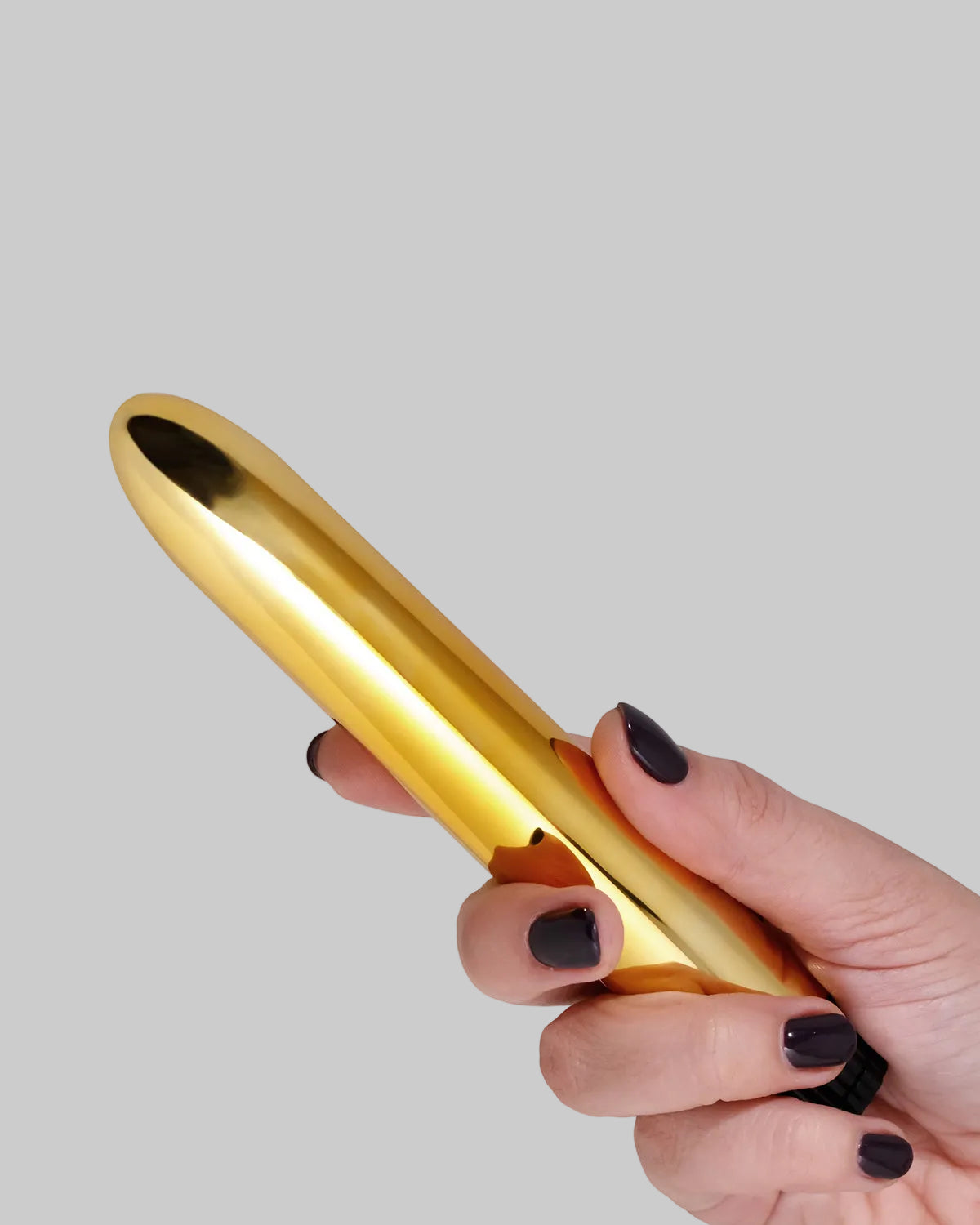 Złoty vibrator trzymany w dłoni z czarnymi paznokciami na szarym tle