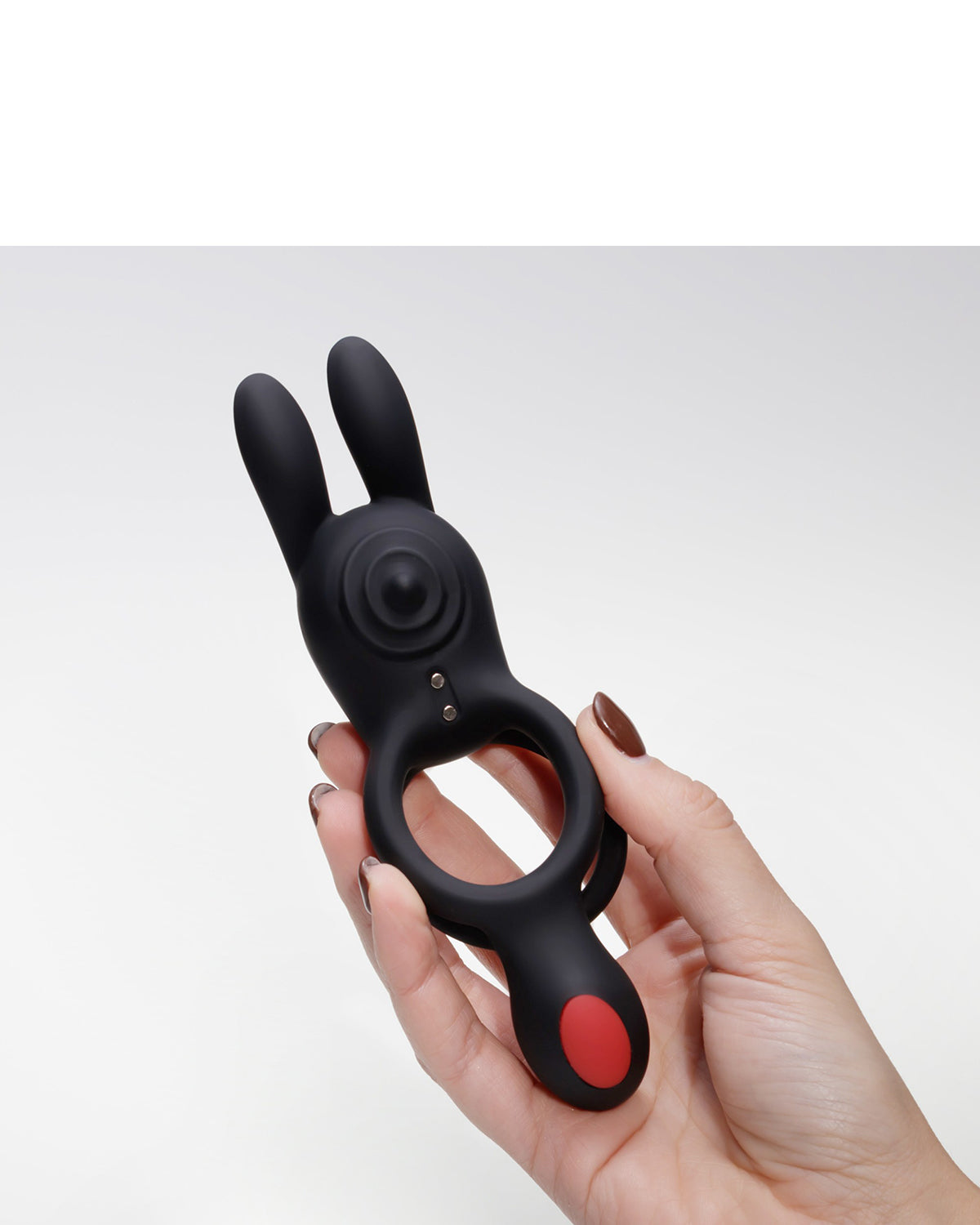 Dłonie trzymające czarny silikonowy pierścień z dwoma wypustkami i czerwonym przyciskiem kontrolnym